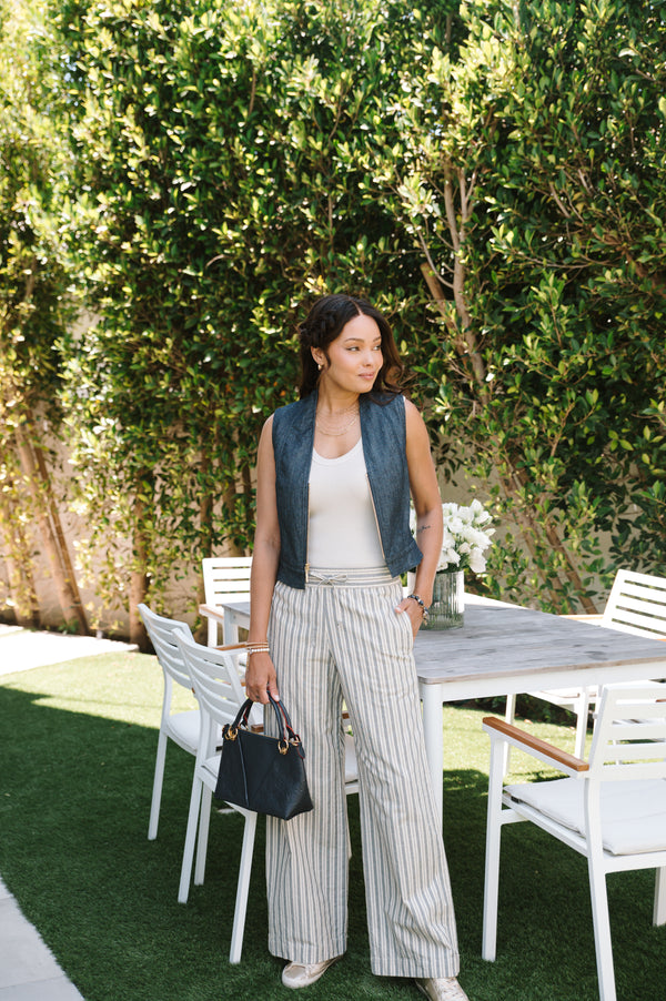 Woman standing outdoors near a dining table with chairs, holding a black handbag.