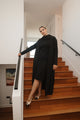 Woman in a black outfit standing on wooden stairs in a modern interior setting