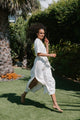 Woman in a white outfit walking on grass with trees in the background