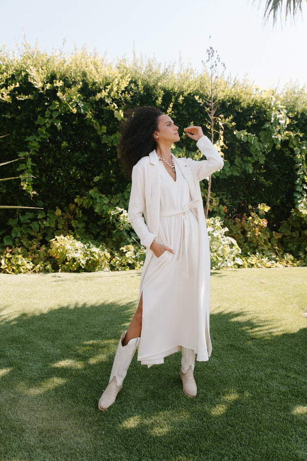 Woman in a white dress standing on grass with greenery in the background