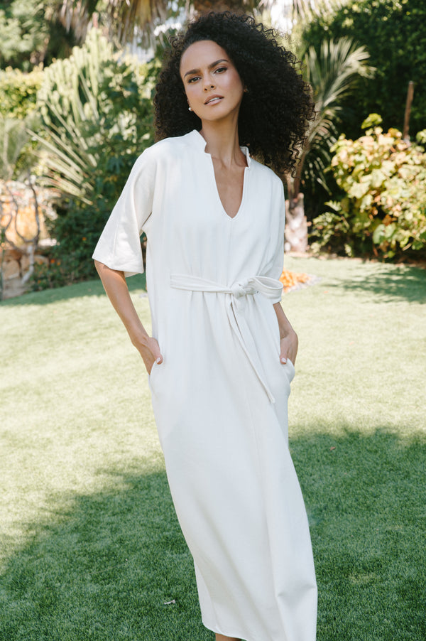 Woman in a white dress standing outdoors with greenery in the background