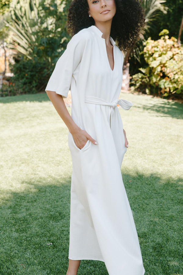 Woman wearing a white dress standing on grass with greenery in the background