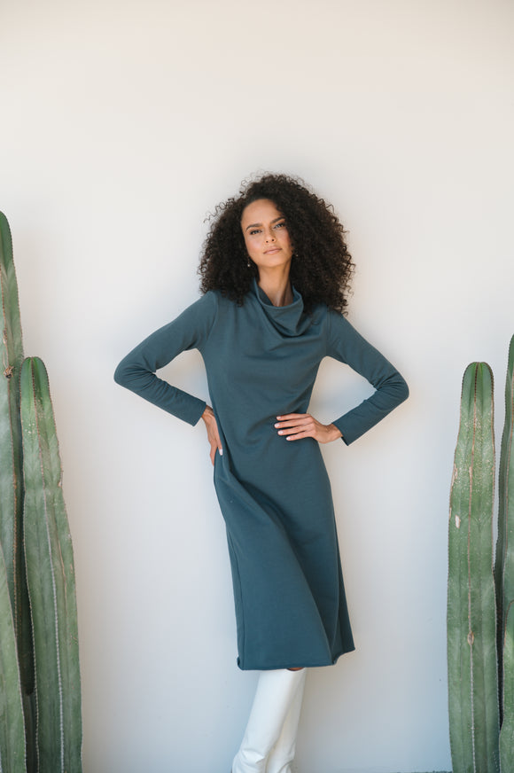 Woman in a grey dress standing between two cacti against a white wall