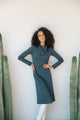 Woman in a grey dress standing between two cacti against a white wall