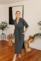 Woman in a grey dress standing in a room with wooden floor and decorative elements.