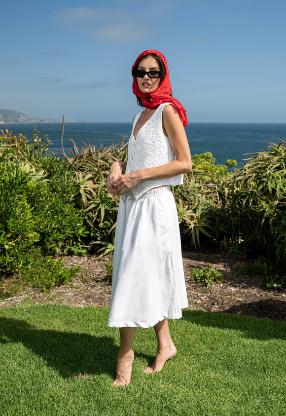 woman wearing white vest and white skirt, with red scarf covering head