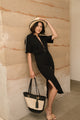 woman wearing long black dress and tan fedora holding tan bag