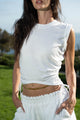 woman wearing white sleeveless shirt, gold chain around waist and white pants
