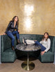 two women, one wearing tan shirt with gold zipper, and pants, the other wearing black leather jacket with jeans