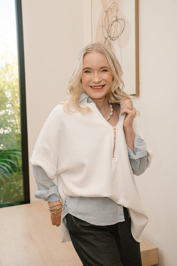 Woman wearing a white poncho over a gray shirt in an indoor setting