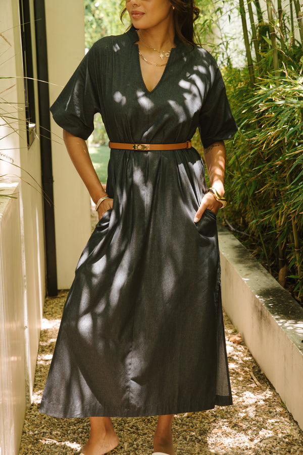 Woman wearing a dark blue dress with a belt, standing outdoors.