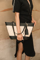 woman wearing long black dress with gold zipper and holding tan bag