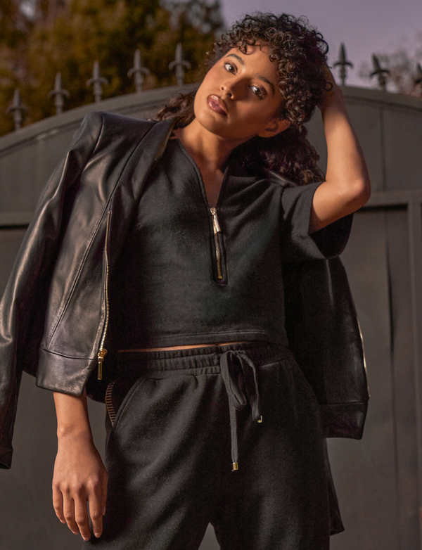 woman wearing black shirt with gold zipper, black pants, and denim jacket hanging on shoulders