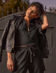 woman wearing black shirt with gold zipper, black pants, and denim jacket hanging on shoulders