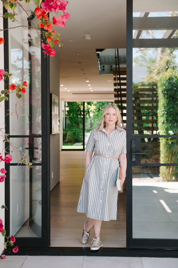 Woman in a striped dress standing in a modern home entrance with flowers on the left.