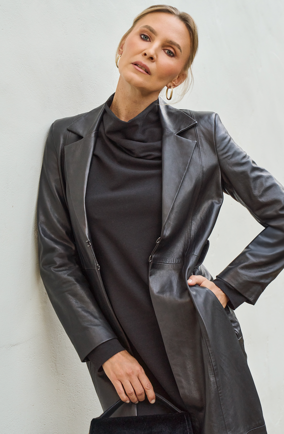 Woman wearing a black leather coat over a black outfit against a light background