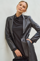 Woman wearing a black leather coat over a black outfit against a light background