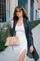 woman wearing short white dress with navy overcoat, holding tan bag