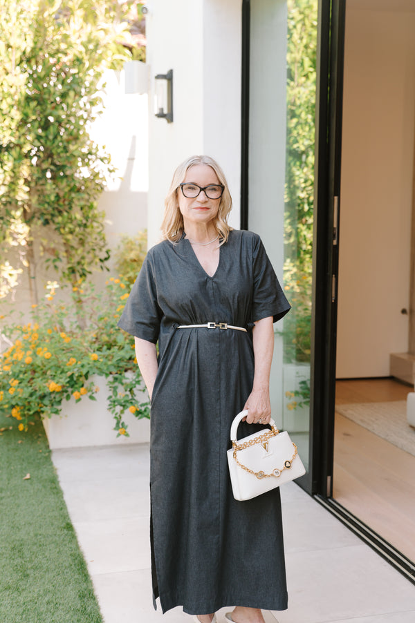 Woman in an indigo dress holding a white handbag outdoors.