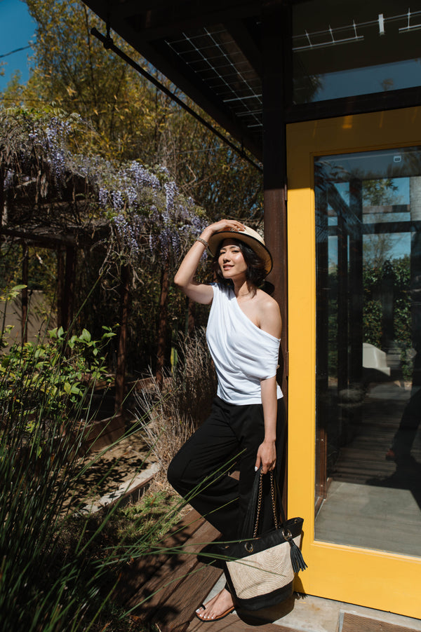 woman wearing white shirt, black pants and tan fedora holding tan bag
