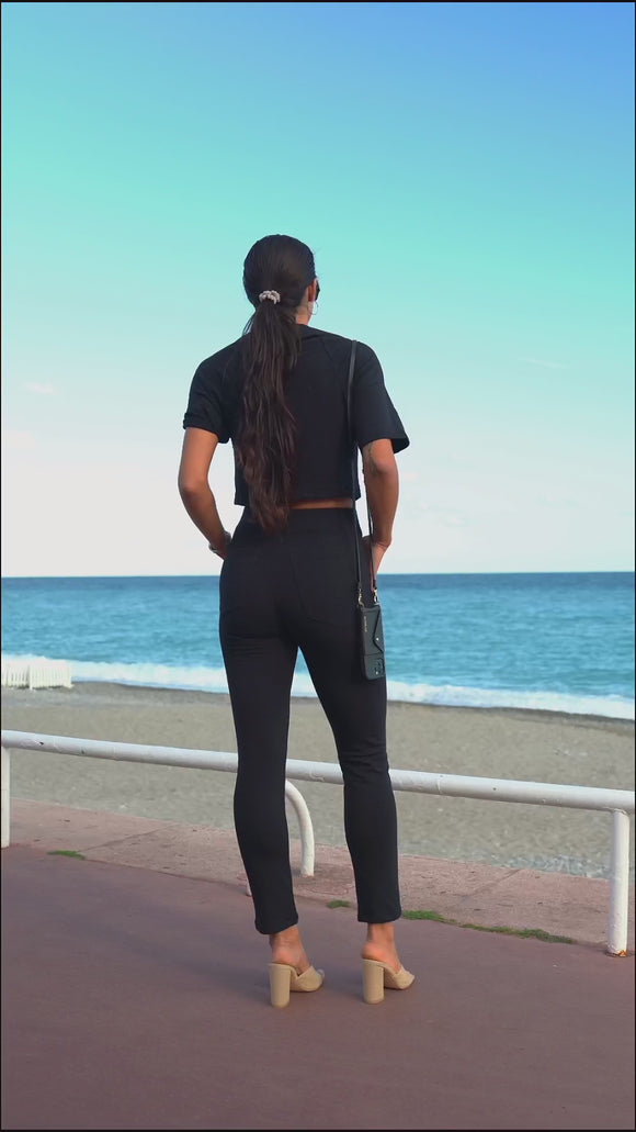 video of woman wearing black shirt and black pants, with black sunglasses, standing at beach
