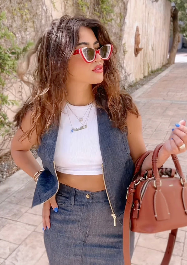 woman wearing white crop top, denim vest and denim skirt holding brown bag