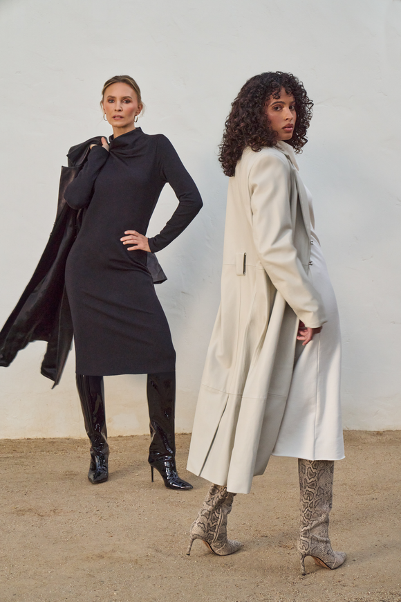 Two women wearing white and black dresses with coats against a white wall