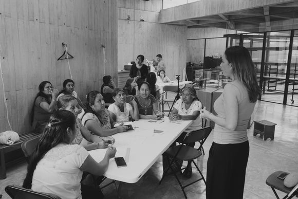 A standing woman gives a speech to a group of other women sitting behind a table