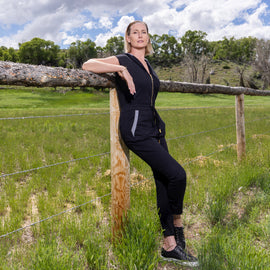 Woman in LPC black jumpsuit leaning against a wooden fence 