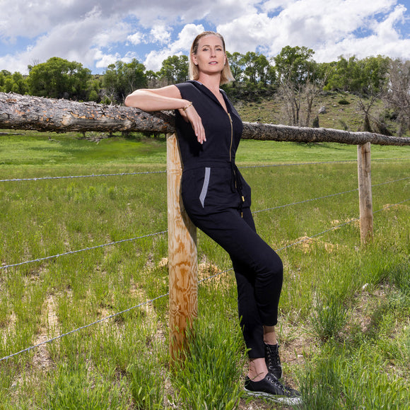 Woman in LPC black jumpsuit leaning against a wooden fence 