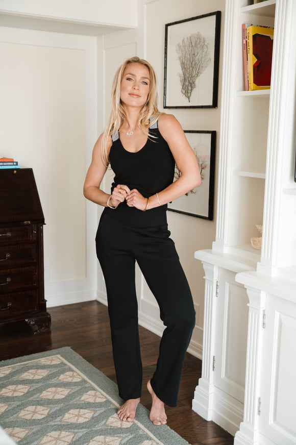 Woman in black outfit standing in a room with wooden floor and white walls.