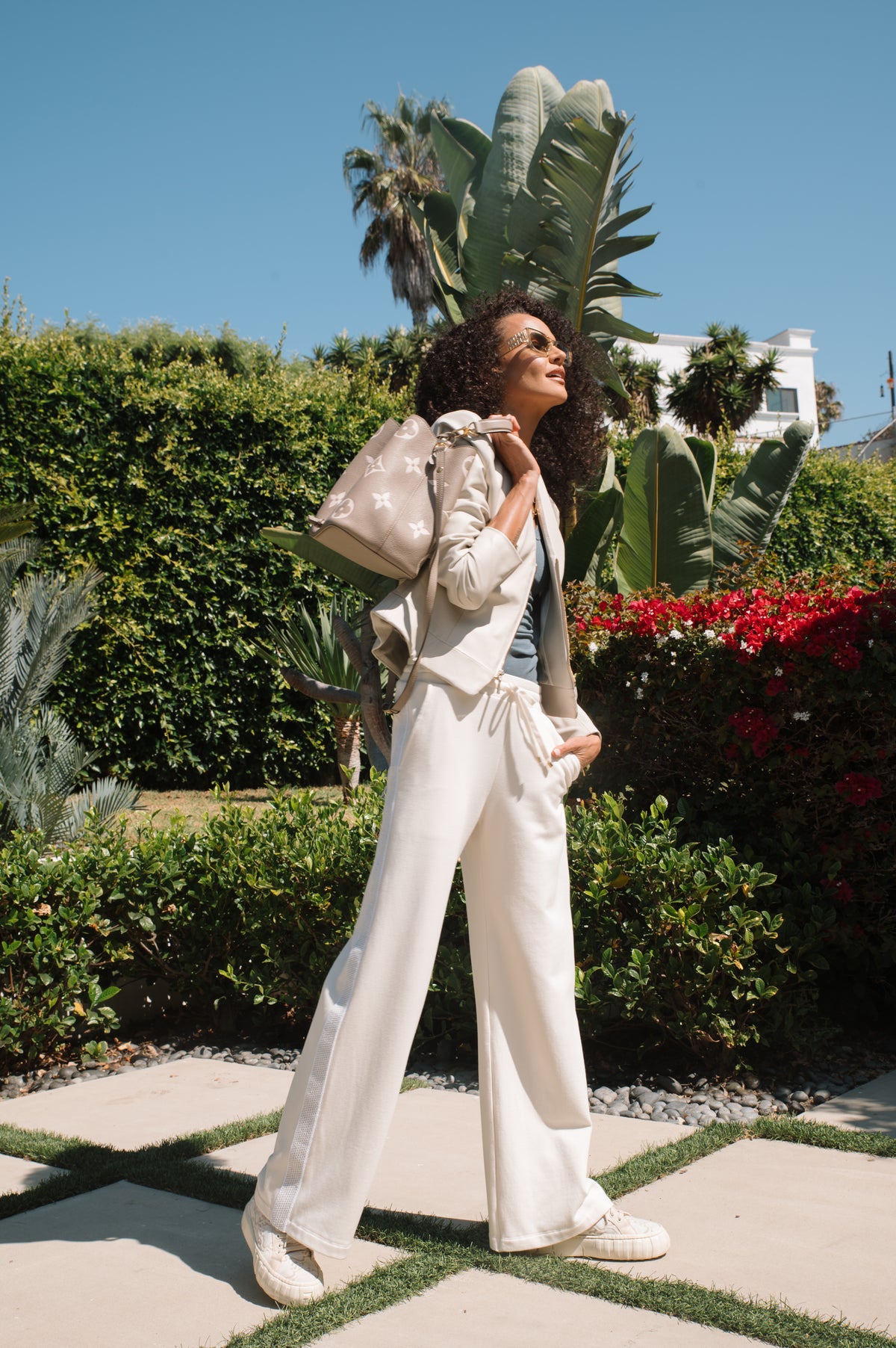 Woman in a stylish outfit standing in a garden with greenery and flowers.