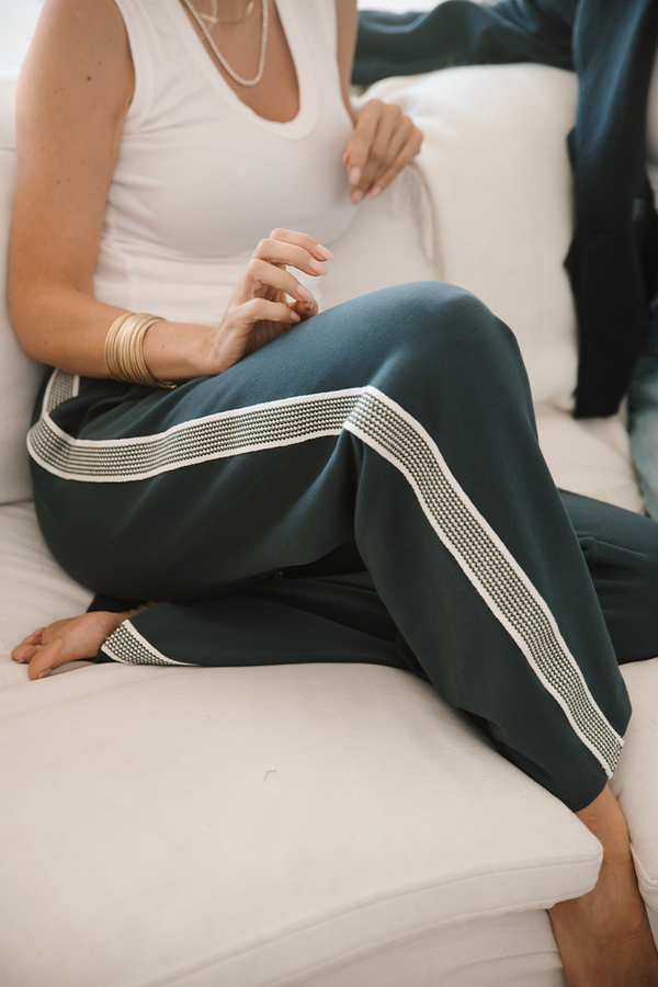 Person wearing grey pants with a white stripe down the pant leg sitting on a white couch.
