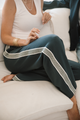 Person wearing grey pants with a white stripe down the pant leg sitting on a white couch.