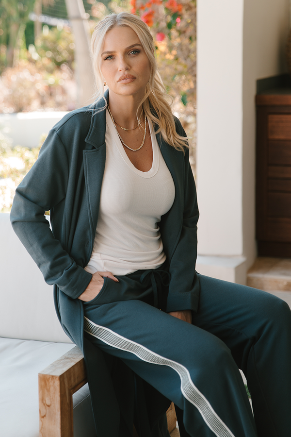 Woman wearing a grey tracksuit with white stripes sitting outdoors.