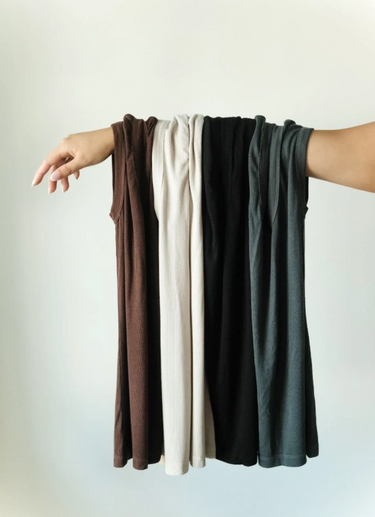 Four different colours of tank tops hanging on an arm against a white background