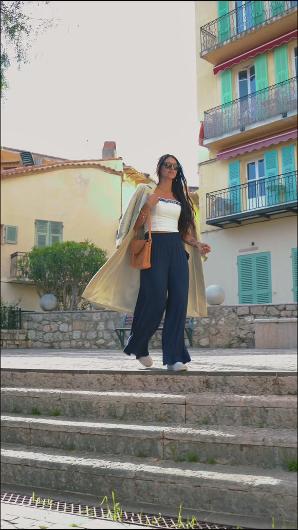video of woman wearing white tube top, navy blue pants, and tan overcoat, with black sunglasses and brown bag